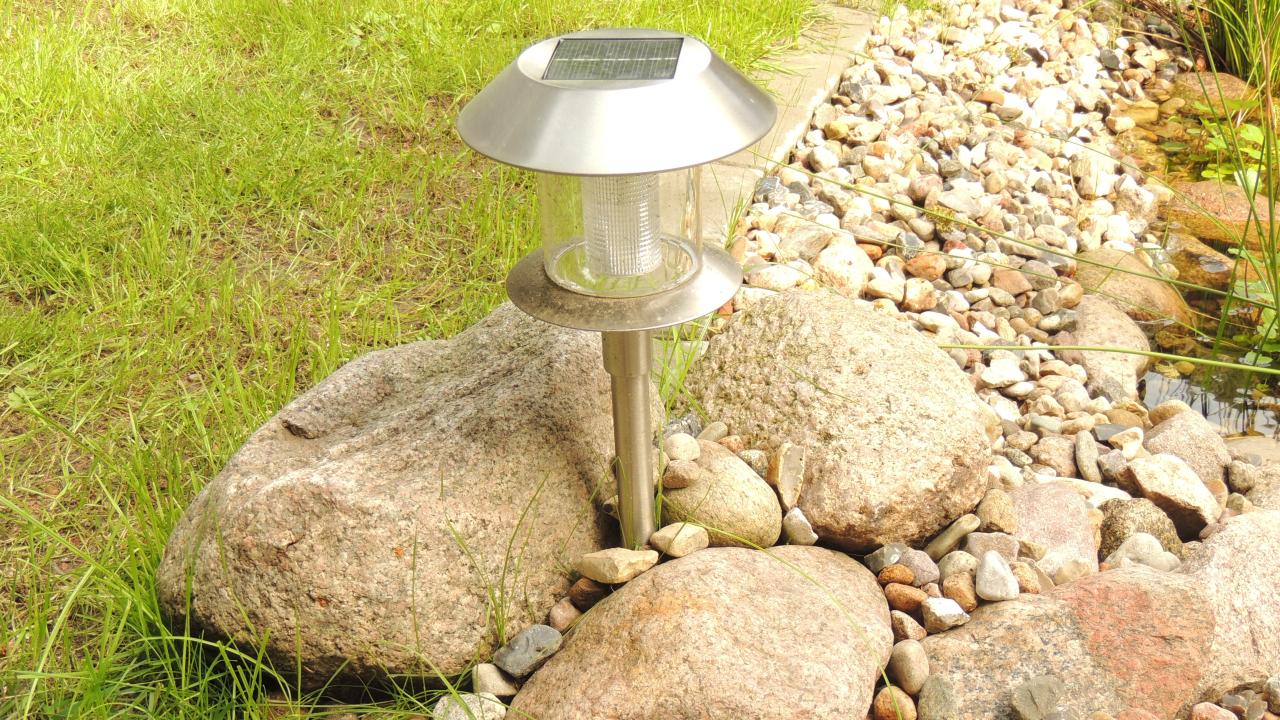 Eine Solarleuchte, die am Teichrand und Bachlauf zwischen drei großen Steinen steht